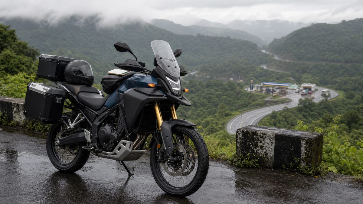 Unbranded middleweight adventure motorcycle on a wet mountain highway near a distant fuel stop